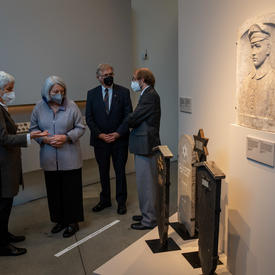 Their Excellencies are in a museum observing a piece of art. They are each speaking with someone respectively. 