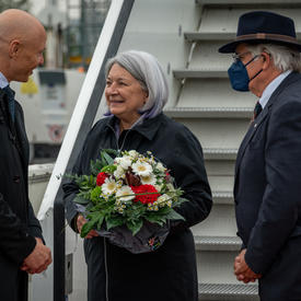 Governor General Mary May Simon, Mr. Whit Grant Fraser and Dr. Philipp Nimmermann are talking at the foot of a flight of stairs. Governor General May Simon is holding a bouquet.