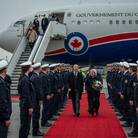 Governor General Mary May Simon and Dr. Philipp Nimmermann, Representative of the Federal State of Hessen, are walking along a red carpet. There is a line of military officers lining both sides of the red carpet.