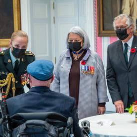  La gouverneure générale Mary May Simon parle à un ancien combattant canadien. Il porte son uniforme et la gouverneure générale porte des décorations militaires et un coquelicot.