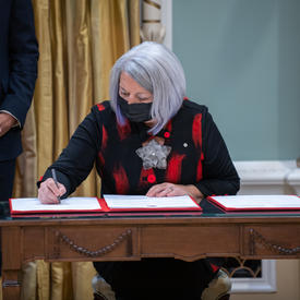 La gouverneure générale Mary May Simon est assise à une table et signe un livre.