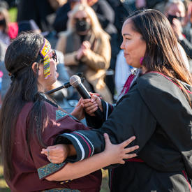 Two women are facing each other with arms linked. They are engaged in throat singing.