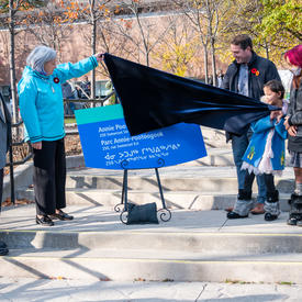 The Governor General unveils a sign for the Annie Pootoogook Park. A man stands to her right. A small group stands on the other side of the sign.