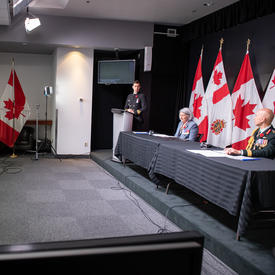 La gouverneure générale Mary Simon est assise à une longue table avec le général Wayne Eyre. Derrière eux, il y a des drapeaux canadiens et des Forces armées canadiennes.