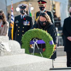 The 2021 National Silver Cross Mother lays a wreath at the Tomb of the Unknown Soldier at the National War Memorial. There are three men in military uniforms standing behind her.