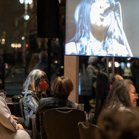 Audience, including Governor General Mary Simon and Buffy Sainte-Marie, watching a video screen of a Buffy Sainte-Maire performance.