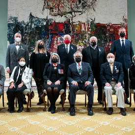 Un groupe de onze personnes, six personnes assises et cinq personnes debout derrière, pose pour une photo devant une grande peinture.