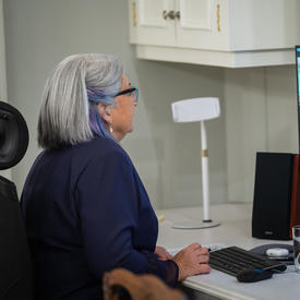 The Governor General participates in a virtual call on her computer. She is sitting at a desk. We can see both her and another woman on her computer screen.