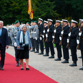 The Governor General and President of Germany are walking on a red carpet at Schloss Bellevue. There are people in military uniform standing along the red carpet.