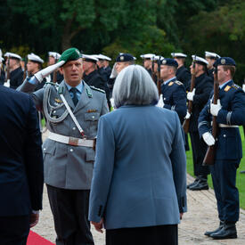 The Governor General and President of Germany are walking on a red carpet at Schloss Bellevue. There are people in military uniform standing along the red carpet.