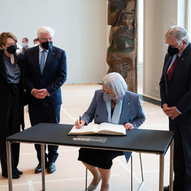 Her Excellency is sitting at a desk signing a book.