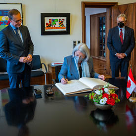 Her Excellency is sitting at a desk signing a book.