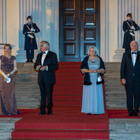 Their Excellencies stand on the red carpet with two other people in formal evening attire at the entrance to a building.