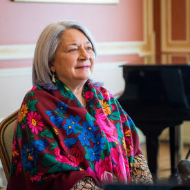 La gouverneure générale Mary Simon est assise. Elle porte un magnifique foulard multicolore. Un piano est visible à l'arrière-plan.