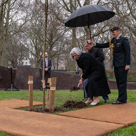 Governor General Mary Simon placing a shovel of dirt at the base of a tree.