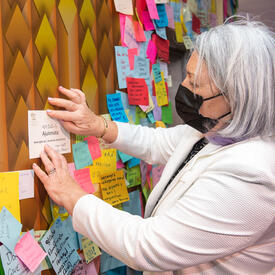 La gouverneure générale Mary Simon place son message à côté des autres sur un mur au pavillon de l'Ukraine. Le mur est couvert de post-it multicolores.