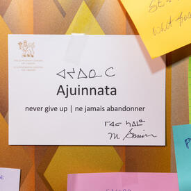 Écrit sur un papier blanc sont les mots «Ajuinnata. Never give up / ne jamais abandonner». On y trouve également la signature de la gouverneure générale Mary Simon ainsi que la traduction en inuktitut.
