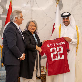 La gouverneure générale Mary Simon et Son Altesse le cheikh Khalid bin Khalifa bin Abdulaziz Al Thani tiennent un chandaille rouge sur lequel est inscrit « Mary Simon 22 ». M. Whit Fraser est debout à côté d’eux.