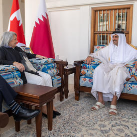 Le gouverneur général Simon et M. Whit Fraser rencontrent l’émir du Qatar. Il y a un drapeau du Qatar et un drapeau du Canada derrière eux.