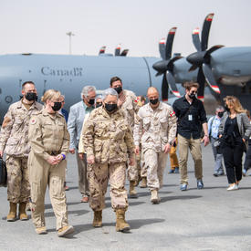 La gouverneure générale et un groupe de personnes marchent vers Camp Canada. Un avion militaire est derrière eux.