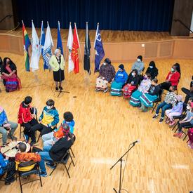 Une vue aérienne du gymnase d’une école. La gouverneure générale Simon et des étudiants sont placés en cercle. La gouverneure générale est debout et parle aux étudiants.
