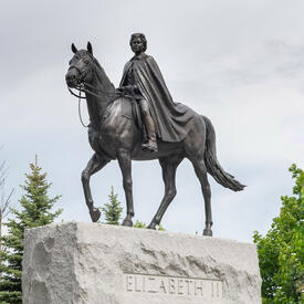 Une grande statue de la Reine à cheval. Le monument repose sur une grande dalle de pierre portant l’inscription « Elizabeth II ».