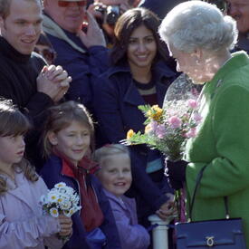 The Queen, wearing a green coat, receives a bouquet of flowers from a group of young children. 