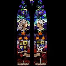 A stained glass window comprising images of Queen Victoria and Queen Elizabeth II, the Royal Crown, their respective cyphers and arms, and two depictions of the Parliament of Canada.