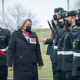 Governor General Mary Simon is walking in front of military members in uniform. She is inspecting the Royal 22e Regiment.
