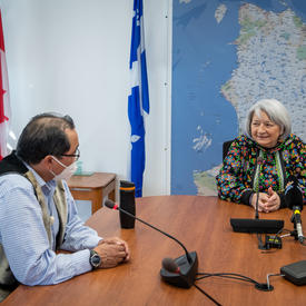 La gouverneure générale est assise à une grande table de conférence. Elle parle avec un homme.