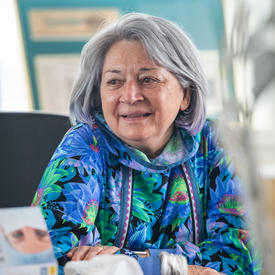 La gouverneure générale est assise à une table, souriante.