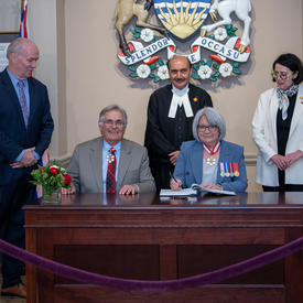 Their Excellencies are sitting behind a table. Premier of British Columbia, John Horgan, Speaker of the Legislative Assembly of British Columbia, Raj Chouhan, and Lieutenant Governor, Janet Austin are standing.