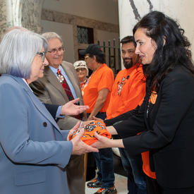 Une femme remet au gouverneure générale Simon un chandail orange.