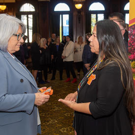 La gouverneure générale s'entretient avec une femme portant un insigne d’un chandail orange.