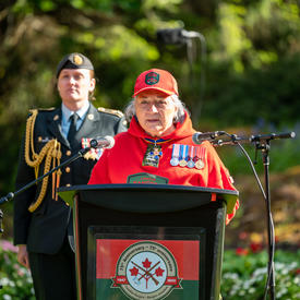 Governor General Simon is standing at a podium. She is speaking into a microphone. She is wearing a Canadian Rangers uniform. A woman wearing a military uniform is standing behind her. 