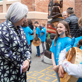 The Governor General is speaking with young kids in a playground. The kids are wearing blue shirts.