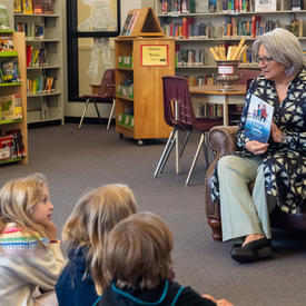 La gouverneure générale Simon présente un livre à un groupe d'enfants. Ils sont assis dans une bibliothèque.