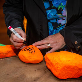 Governor General Simon is writing on an orange stone. The message reads, “Let’s walk together.” There is a line in Inuktitut under the English sentence.