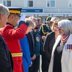 A man in uniform is saluting the Governor General as she greets a row of people.