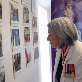 The Governor General is looking at a wall of photos.