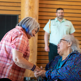 Governor General Simon is shaking hands with a person sitting in front of her. A man wearing a military uniform is standing in the background.