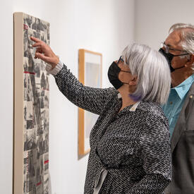 Her Excellency is pointing at a photo that is part of a collage on a wall.