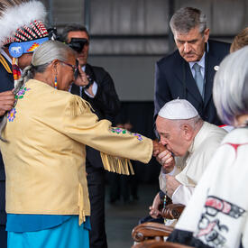 Deux personnes sont debout devant le Pape François. Le pape François embrasse une de leurs mains.