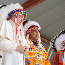 Pope Francis is wearing an Indigenous headdress. Indigenous leaders are standing around him.