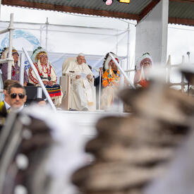 Pope Francis is seated on stage with Indigenous leaders.