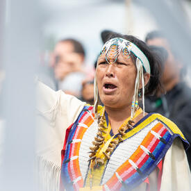 Une femme vêtue d'une tenue traditionnelle autochtone pousse un cri.
