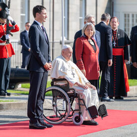 La gouverneure générale Simon et le premier ministre Justin Trudeau sont debout de part et d'autre du pape François, assis dans un fauteuil roulant. Ils sont sur un tapis rouge.