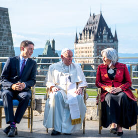 Governor General Simon, Prime Minister Justin Trudeau and His Holiness Pope Francis are sitting next to each other outside of the GGCitadelle. The Chateau Frontenac is in the distance behind them.