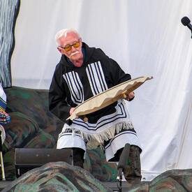 A man wearing traditional Inuit clothing plays a qilaut. 