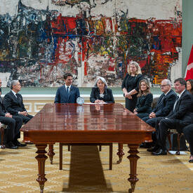 Le premier ministre, la gouverneure générale et un groupe de ministres sont assis dans la grande salle de bal de Rideau Hall.